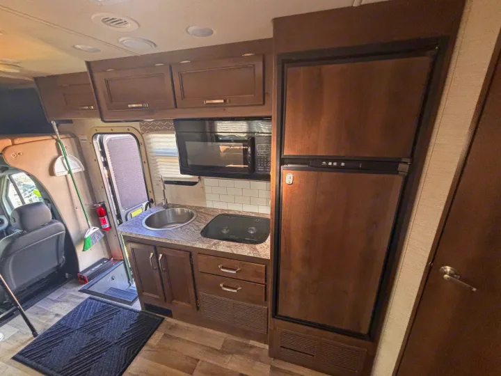 Inside an RV rental, a compact kitchen with microwave, sink, stove, fridge, and cabinets, near the entrance with safety items.. Jayco Melbourne 2020