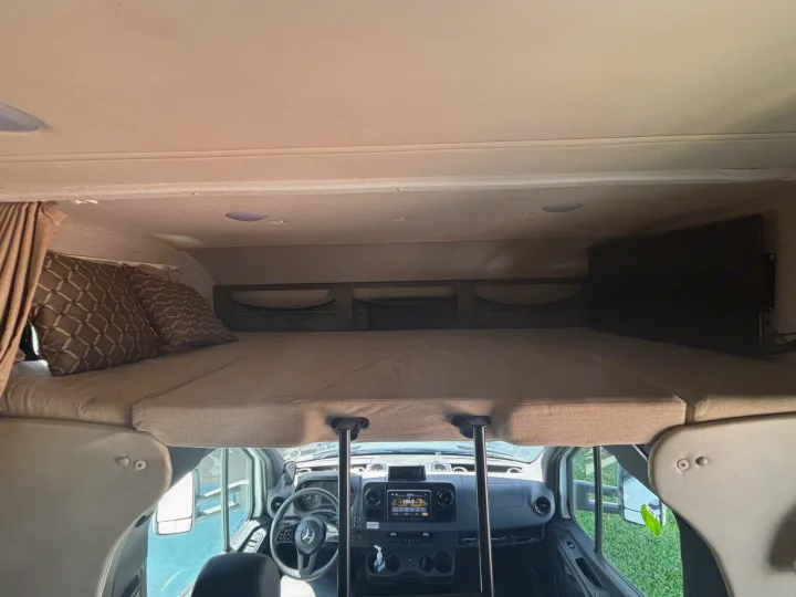 RV rental interior: A cozy cab-over bed with a TV, overlooking the Mercedes-Benz driver's cabin.. Jayco Melbourne 2020