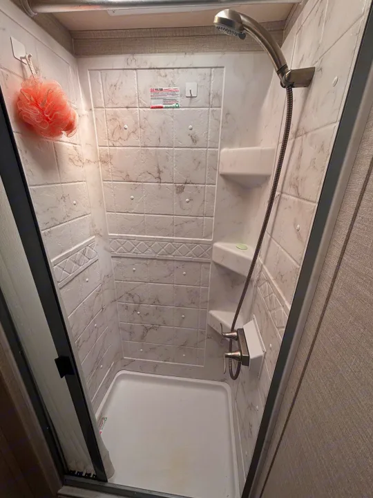RV rental shower: compact and clean with faux marble walls, built-in shelves, and a handheld showerhead. Ideal for travel.. Jayco Melbourne 2020