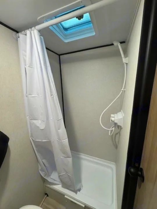 Compact RV rental shower features a white curtain, handheld showerhead, shower pan, and a skylight for natural light.. Keystone RV Coleman 13B 2025