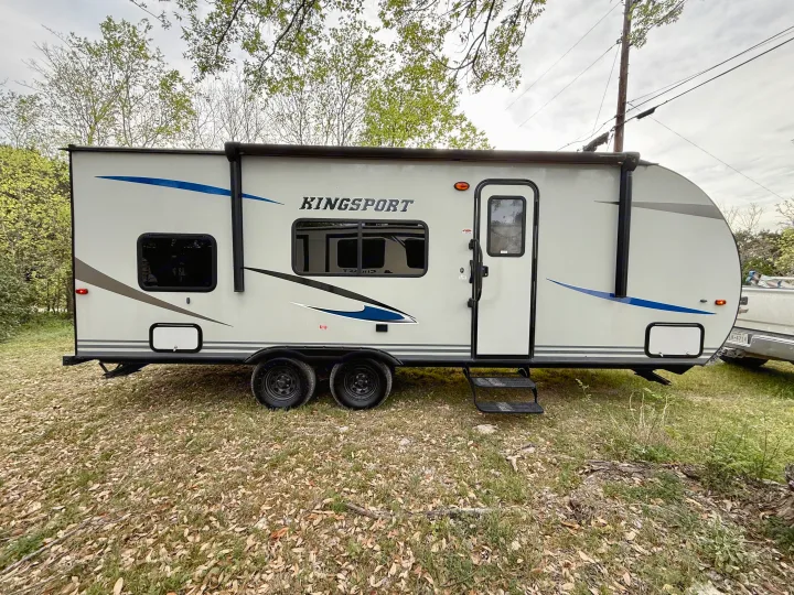 Light-colored Kingsport travel trailer RV rental, with blue accents, dual axles & awning, parked on grass for your adventure.. Gulf Stream Kingsport 2021