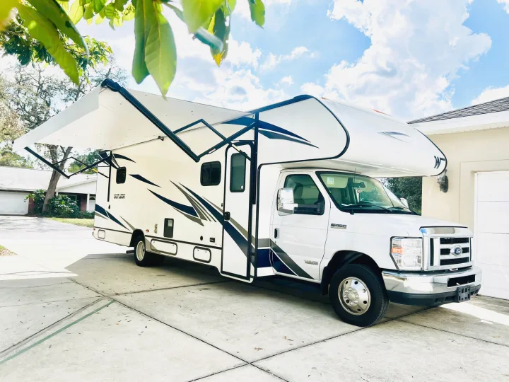 White RV rental parked on a driveway with an extended awning under a sunny sky. Perfect for your next road adventure!. Winnebago Outlook 2020