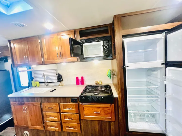This clean RV rental kitchen offers a stove, open microwave, sink, open fridge, and ample wooden cabinets for your road trip.. Winnebago Outlook 2020