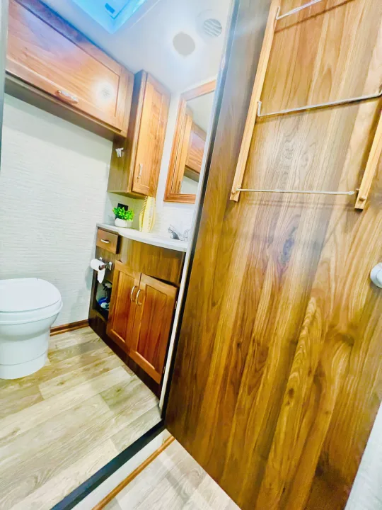 RV rental bathroom with toilet, wood vanity & cabinets, and a door featuring useful hanging rods for storage.. Winnebago Outlook 2020