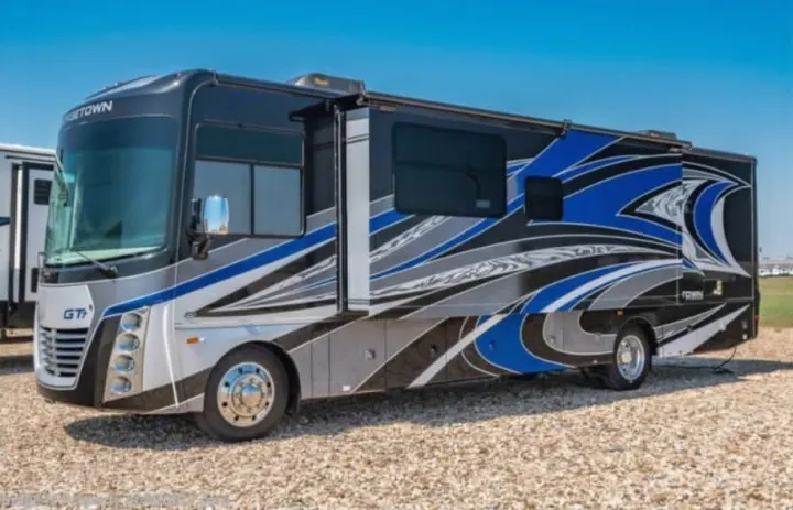 This sleek Georgetown Class A motorhome, ideal for an rv rental, showcases a vibrant black, blue, and grey design outdoors.. Georgetown GT7 2022