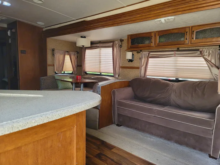 Comfortable RV rental interior featuring a living area with a sofa, dinette seating, and a kitchen counter.. Forest River Wildwood Heritage Glen Lite 2014