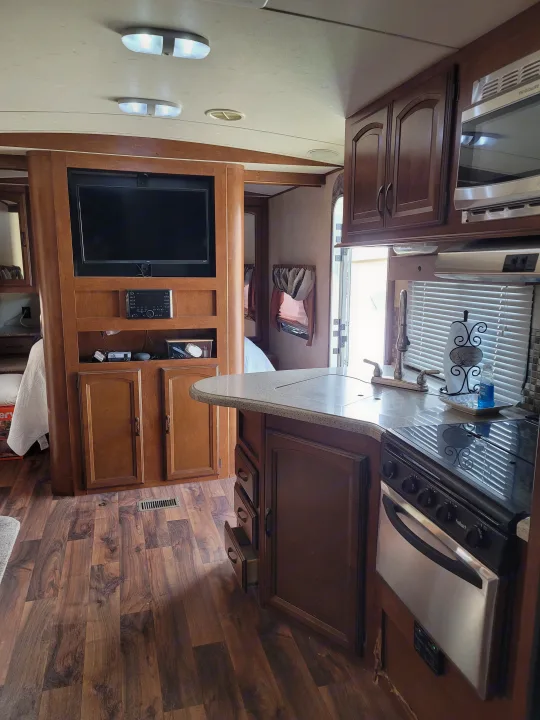 Cozy RV rental interior featuring a living area with TV, and a compact kitchen with wood cabinets and light counters.. Forest River Wildwood Heritage Glen Lite 2014