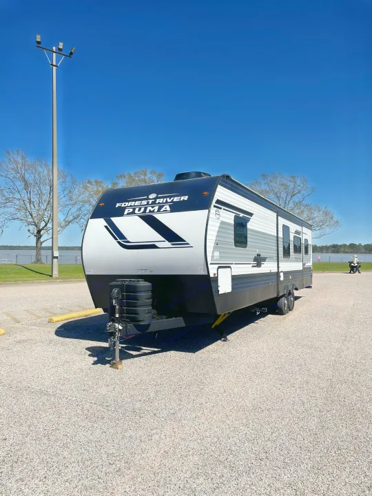 Forest River Puma RV rental parked on a gravel lot by a lake under a clear blue sky.. Palomino Puma 337BH 2025
