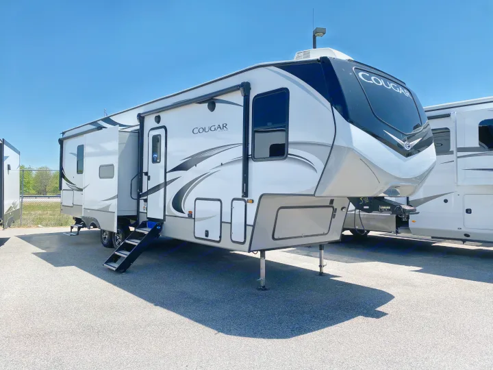 Explore this modern white Cougar fifth-wheel RV available for rental, parked outdoors with slide-outs extended.. Keystone RV Cougar 2021