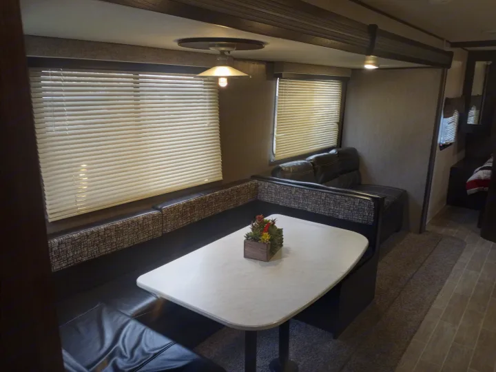 Inside an RV rental: Dinette with black upholstered U-shaped bench, white table, and bright windows with blinds.. Trail Runner heartland 25sle 2016