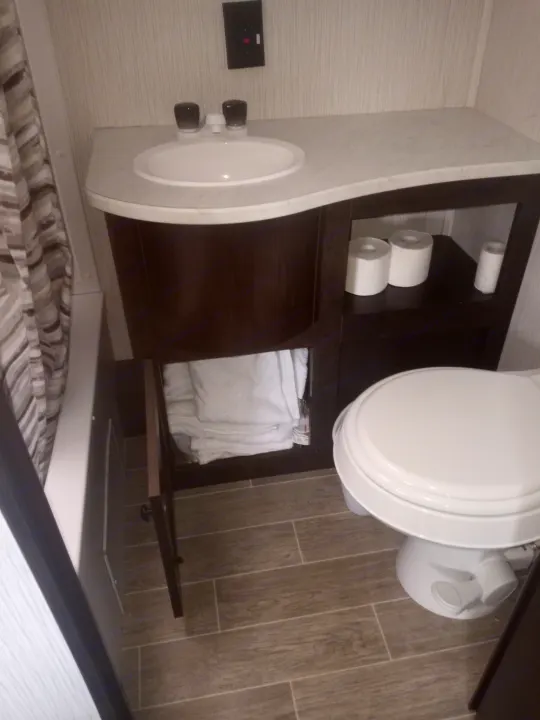 Compact RV rental bathroom: features a vanity with sink, a toilet, plus storage for towels and toilet paper rolls.. Trail Runner heartland 25sle 2016