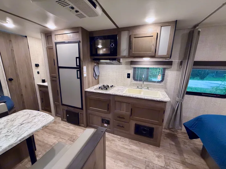 This rv rental interior features a full kitchen with a fridge, microwave, stove, sink, and cabinets, plus a dining table and bed.. Gulf Stream Kingsport 2021