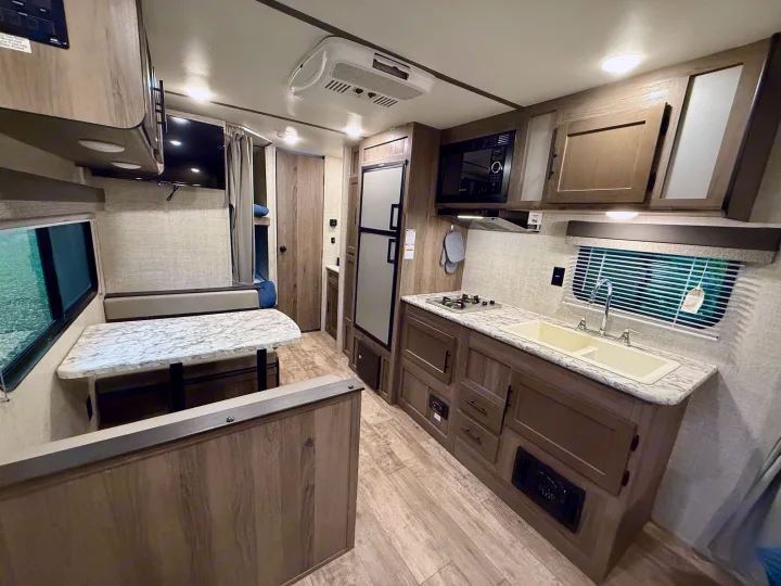 Inside a modern rv rental: kitchen with stove & sink, dinette, fridge, bunk beds & TV. Comfortable for road trips.. Gulf Stream Kingsport 2021