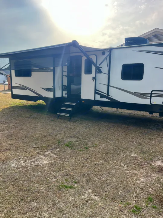White travel trailer RV with extended awning and steps, perfect for your next RV rental. Parked outdoors on a sunny day.. Cruiser RV MPG 2022
