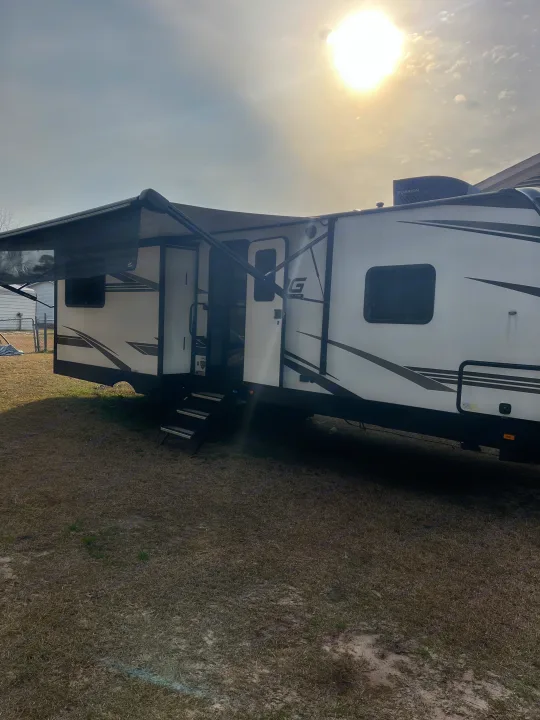 Bright RV rental: A white travel trailer with an extended awning and entry steps, parked outdoors on a sunny day.. Cruiser RV MPG 2022