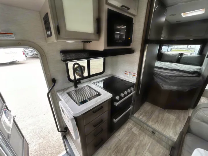 RV rental interior featuring a compact kitchen with sink, stove, microwave, and a cozy bedroom area.. GMC/THOR MAGNITUDE 2025