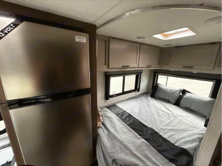 RV rental interior: A compact bedroom featuring a 12-volt refrigerator, bed, overhead cabinets, and windows.. GMC/THOR MAGNITUDE 2025