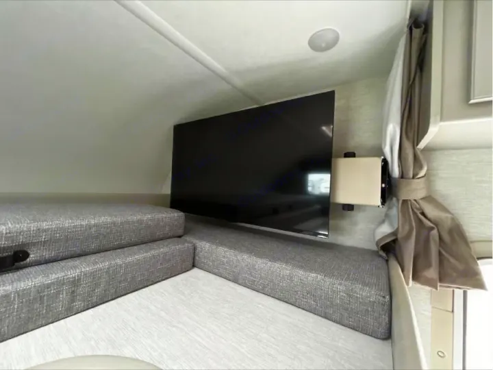 RV rental: Compact interior with gray upholstered cushions, a wall-mounted TV, and tied-back curtains.. GMC/THOR MAGNITUDE 2025