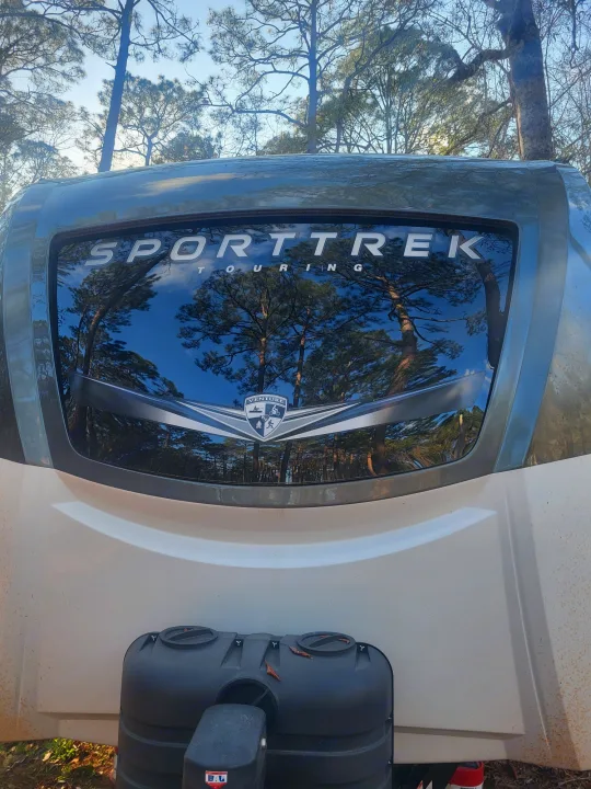 Front view of a SportTrek Touring RV parked in nature, reflecting trees. Ideal for an rv rental trip.. Sporttrek Touring Edition 2024