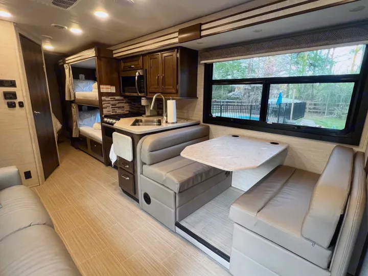 Bright RV rental interior features a kitchen, cozy dinette, bunk beds, and a scenic window view. Ideal motorhome for family adventures.. Entegra Coach Esteem 2021
