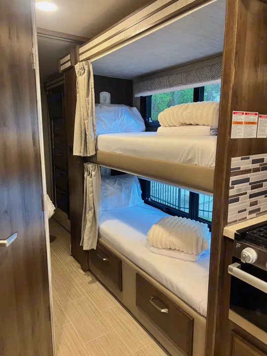 Cozy RV rental bunk beds with fresh white linens, storage drawers, and nearby kitchen setup.. Entegra Coach Esteem 2021