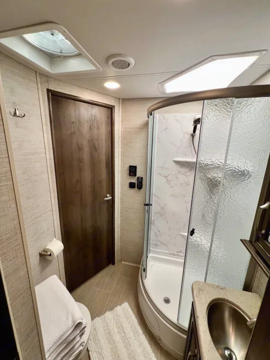Step inside this modern rv rental bathroom with a compact corner shower, toilet, and sink, featuring bright lighting.. Entegra Coach Esteem 2021