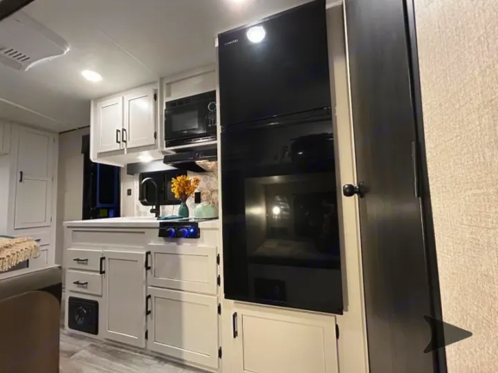 Modern RV rental kitchen features white cabinets, black fridge & microwave. Compact yet functional interior with bunk area visible.. Other Other 2025