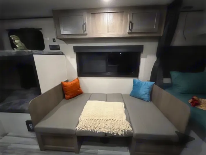 View inside an RV rental, showing a gray dinette area that flattens into a bed, with bunk beds on the left and a main bed on the right.. Other Other 2025