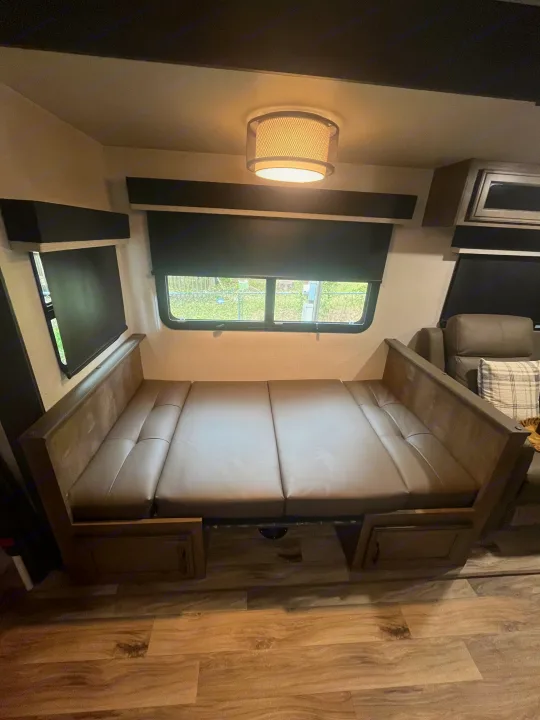 RV rental: Dinette converted to a bed with brown cushions. Features windows with shades, overhead light, and wood-look flooring.. Sporttrek Touring Edition 2024