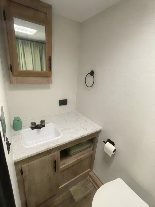 Clean RV rental bathroom with sink, wood vanity, toilet, mirrored cabinet. Shower curtain visible in reflection.. Gulf Stream Ameri-Lite 2024