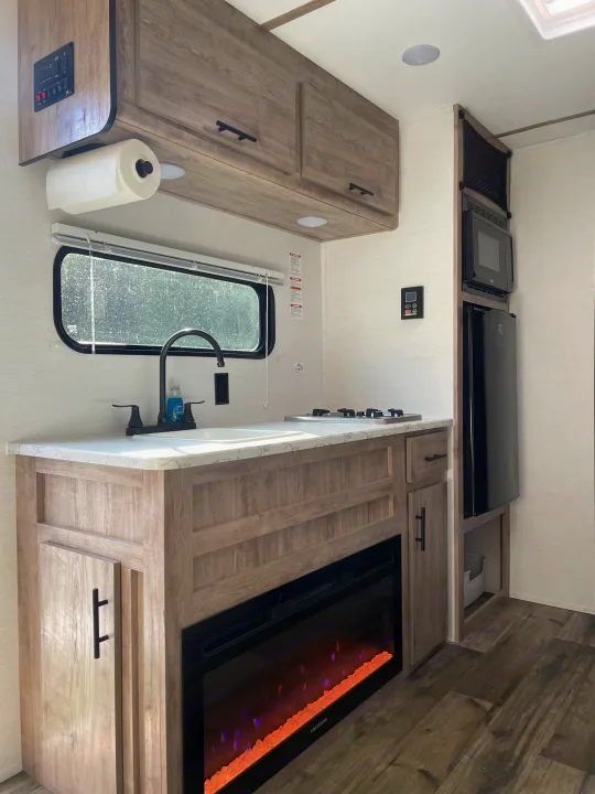RV rental kitchen: modern design with sink, stove, microwave, fridge, & electric fireplace, all in a wood-tone finish.. Gulf Stream Ameri-Lite 2024