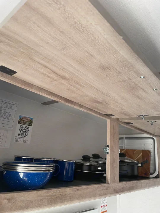 Open RV rental cabinet with blue enamel bowls, pots, and Camp Gulf Stream owner info visible inside.. Gulf Stream Ameri-Lite 2024