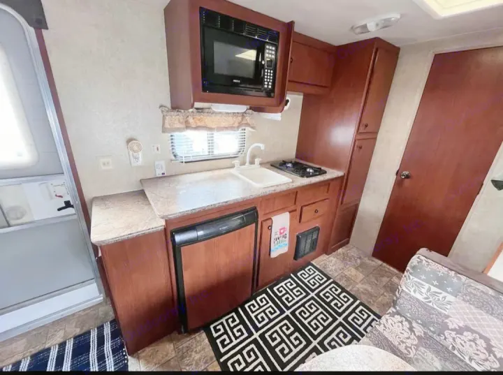Inside an RV rental: compact kitchen with microwave, sink, stove, fridge, and adjacent living space.. Forest River Salem Cruise Lite 2013