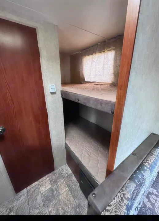 This RV rental features a cozy sleeping area with two bunk beds (mattresses visible), a brown door, and patterned sofa. Ideal camper.. Forest River Salem Cruise Lite 2013
