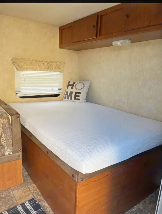 Relaxing RV rental sleeping area featuring a bed with a 'HOME' pillow, window, and ample wooden storage.. Forest River Salem Cruise Lite 2013