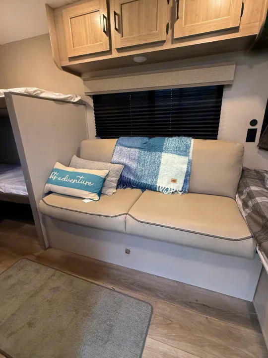 Inviting rv rental interior featuring a beige dinette sofa with pillows, blue blanket, and a bunk bed.. Forest River Coachmen Catalina Summit 2024