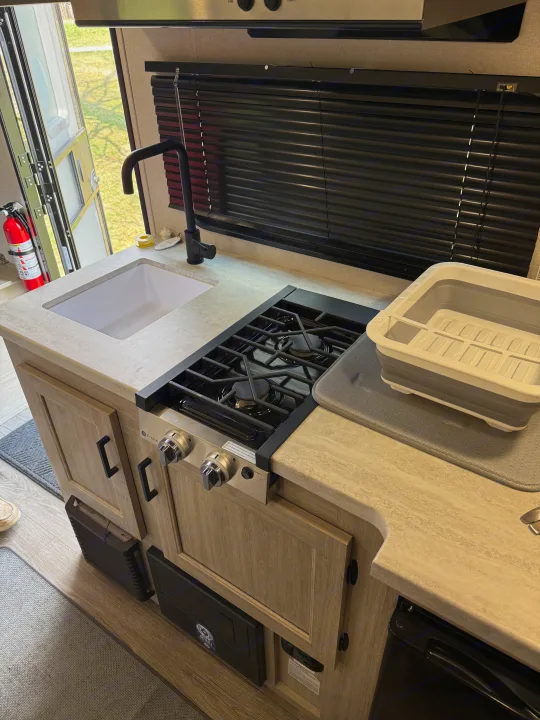 Spacious RV rental kitchen featuring a sink, gas stove, and counter space. An open door reveals the outdoors.. Forest River Coachmen Catalina Summit 2024
