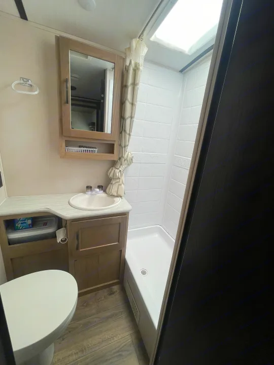 Clean RV rental bathroom featuring a toilet, vanity with sink, medicine cabinet, and bright shower with skylight.. Forest River Surveyor Legend 2019