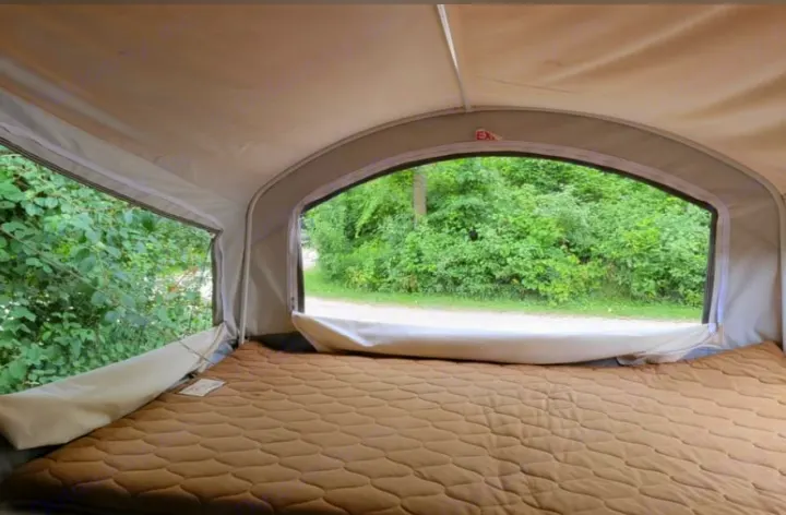 **RV rental** pop-up camper interior: Quilted bed faces large windows with a view of green trees & dirt path.. Forest River Hybrid 16RB 2019