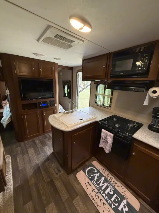 Interior of a cozy RV rental, showing the kitchen area with sink, stove, microwave, and living space with TV. Perfect for road trips!. Keystone RV Bullet Ultra Lite 2017