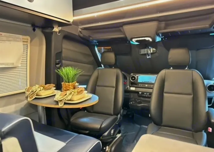 Experience comfort in this RV rental. Interior shows swiveling front seats, a compact dining table, and the driver's dashboard.. Winnebago Revel 2024