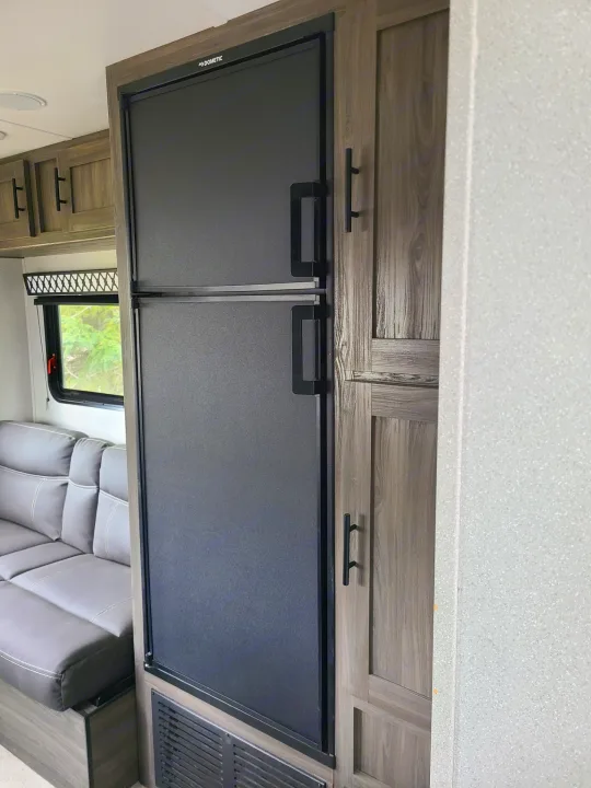 Inside an RV rental: a black Dometic refrigerator, wood-grain cabinets, and a comfy gray sofa await your adventures.. Forest River Shasta 2021