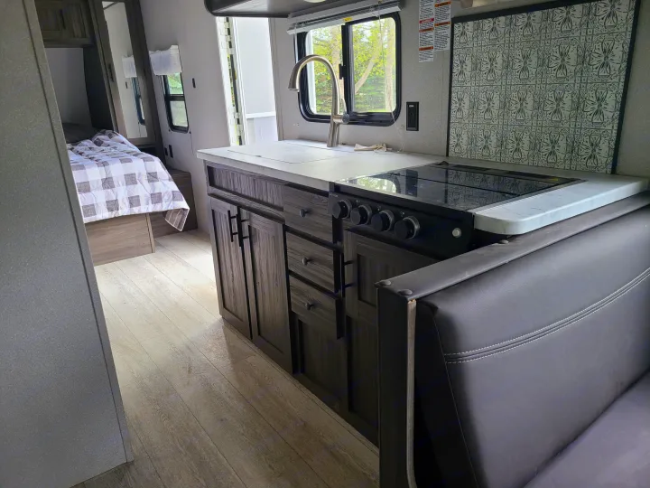 Spacious RV rental interior featuring a modern kitchenette, full bed, & comfy leather-look seating. Light wood floors.. Forest River Shasta 2021