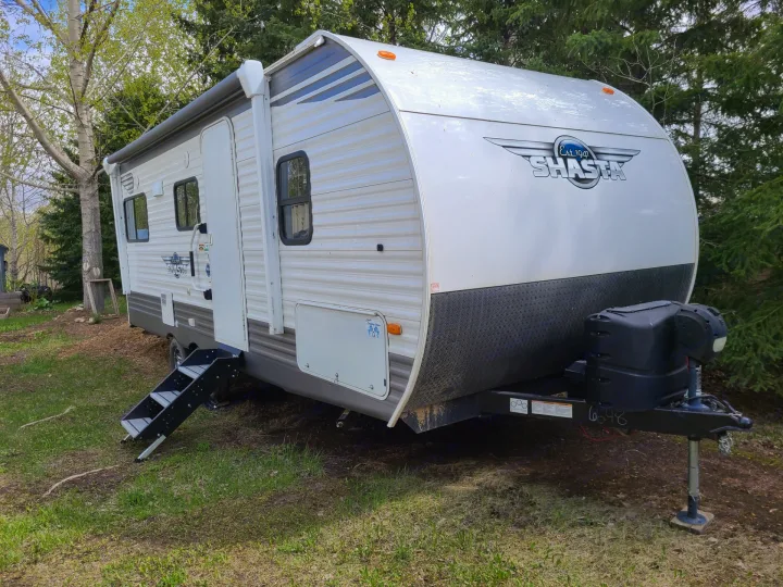 White Shasta travel trailer RV rental, with an awning and steps extended, parked on a grassy outdoor site.. Forest River Shasta 2021