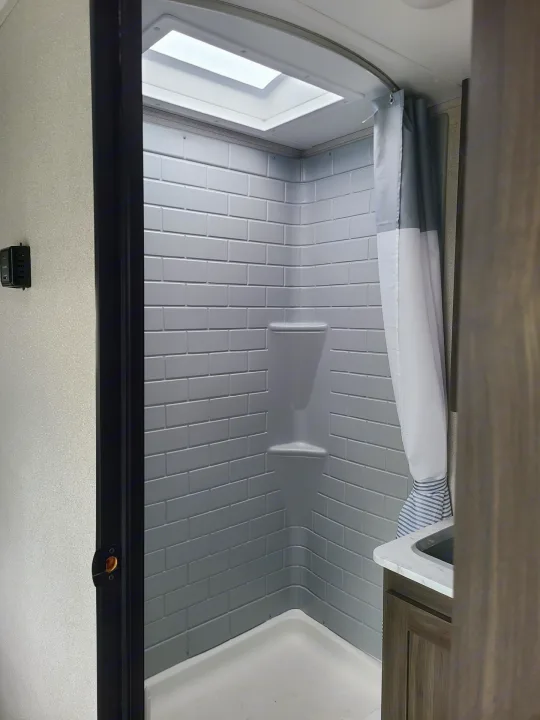 RV rental shower: Bright interior with a skylight, subway-tile look walls, built-in shelves, and a clean curtain. Ideal for travel.. Forest River Shasta 2021
