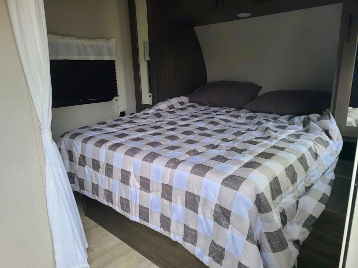 Cozy RV rental bedroom with a plaid comforter, built-in storage, and dark wood accents.. Forest River Shasta 2021