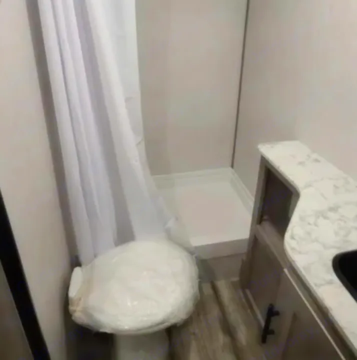 Efficient RV rental bathroom: small shower with curtain, plastic-covered toilet, and sink counter. Ideal for travel.. Dutchmen Coleman Lantern LT 2021