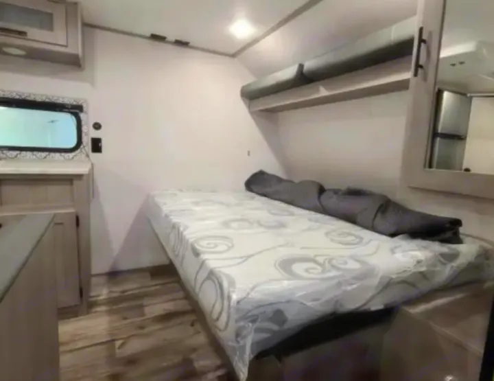 RV rental interior: cozy bedroom with bed, overhead bunk, and a compact living space featuring wood floors.. Dutchmen Coleman Lantern LT 2021