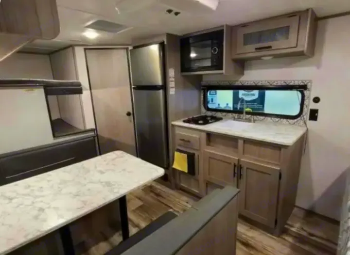 Compact RV rental interior featuring a kitchen with microwave, sink, and stovetop, a dinette, and bunk beds.. Dutchmen Coleman Lantern LT 2021