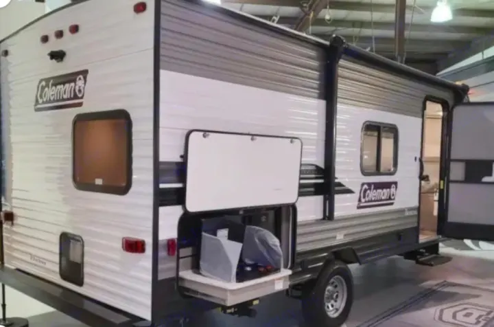 A white and gray Coleman travel trailer (RV) with an open side compartment/outdoor kitchen and entrance door, ideal for rv rental.. Dutchmen Coleman Lantern LT 2021